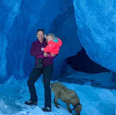 woman with child and dog in front of glacier cave